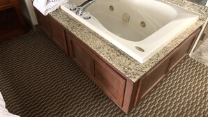 Une salle de bain avec une grande baignoire blanche, des meubles en bois et un comptoir en granit.