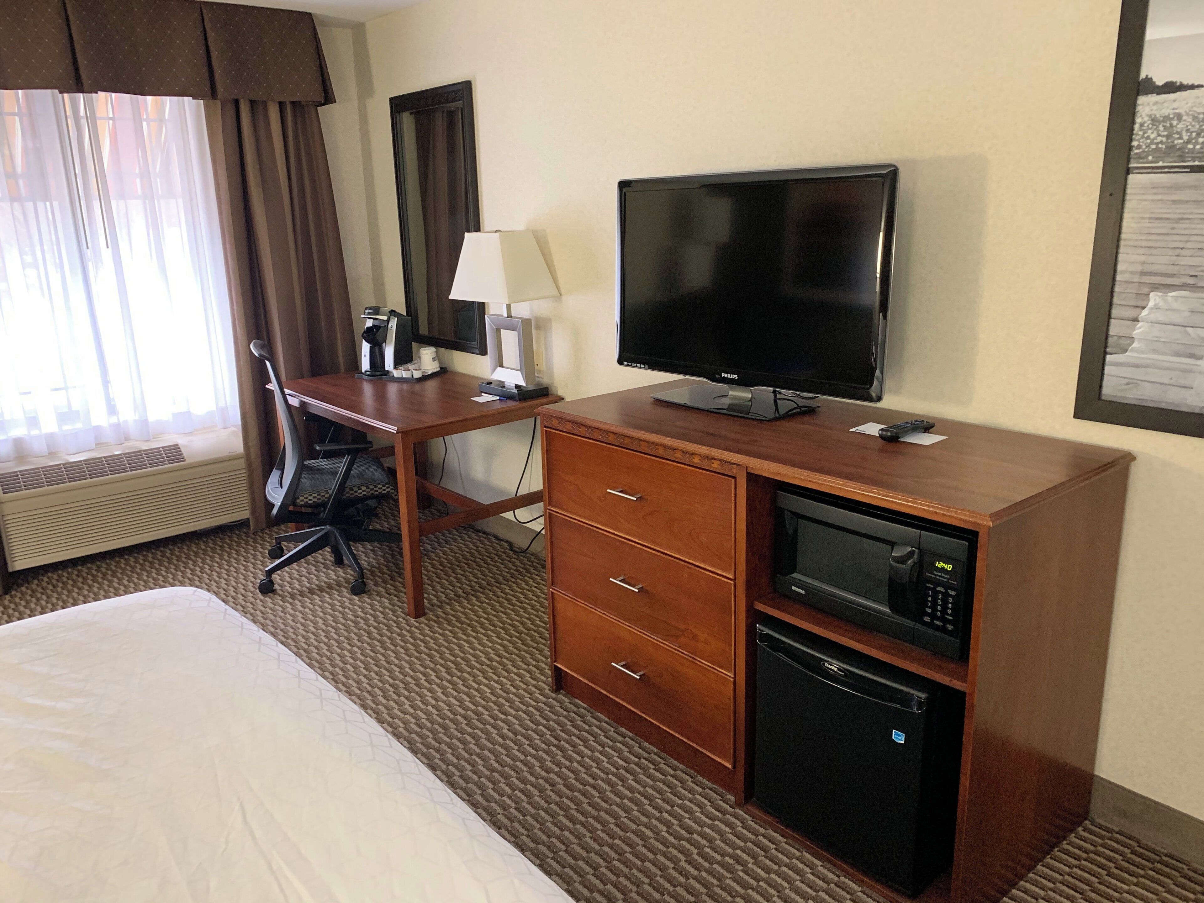 Une chambre d’hôtel équipée d’un lit, d’un bureau avec un ordinateur, d’une télévision, d’un four à micro-ondes et d’un radiateur.