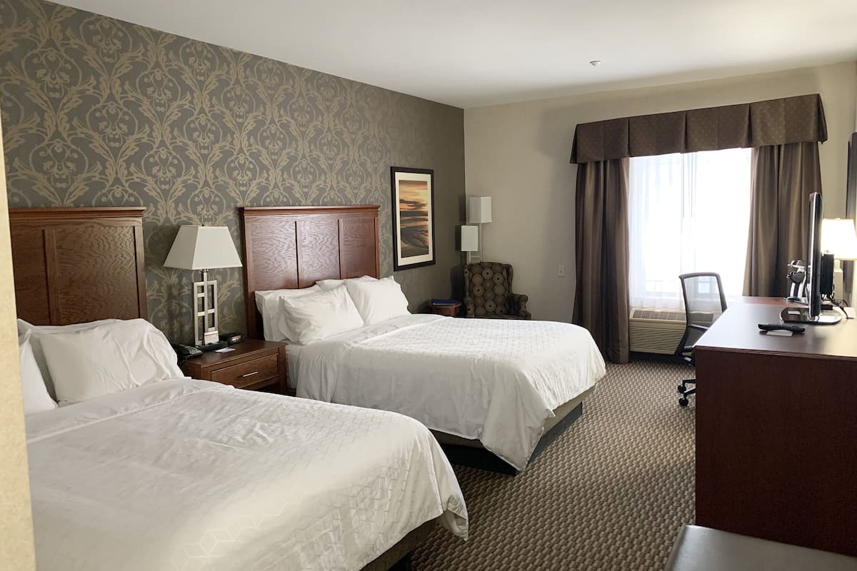 A hotel room with two beds, a desk, a chair, a lamp, and a painting on the wall.