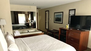 Une chambre d’hôtel avec un grand lit, une salle de bain avec baignoire, un bureau, une télévision et un miroir.