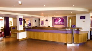 Un espace d’accueil d’hôtel comprenant un comptoir de réception, une enseigne « Premier Inn » et une signalétique indiquant la présence d’installations destinées aux professionnels.