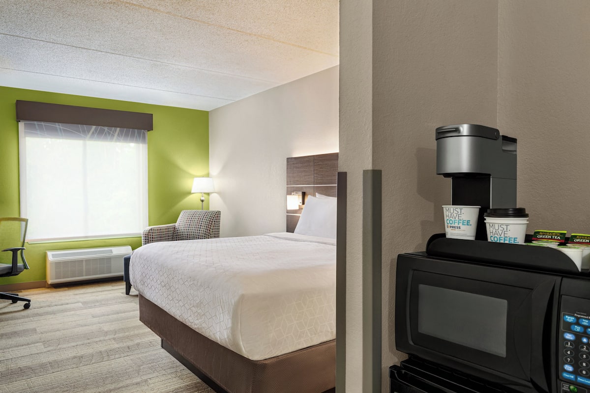 A hotel room with a bed, a desk, a chair, a coffee machine, and a microwave.