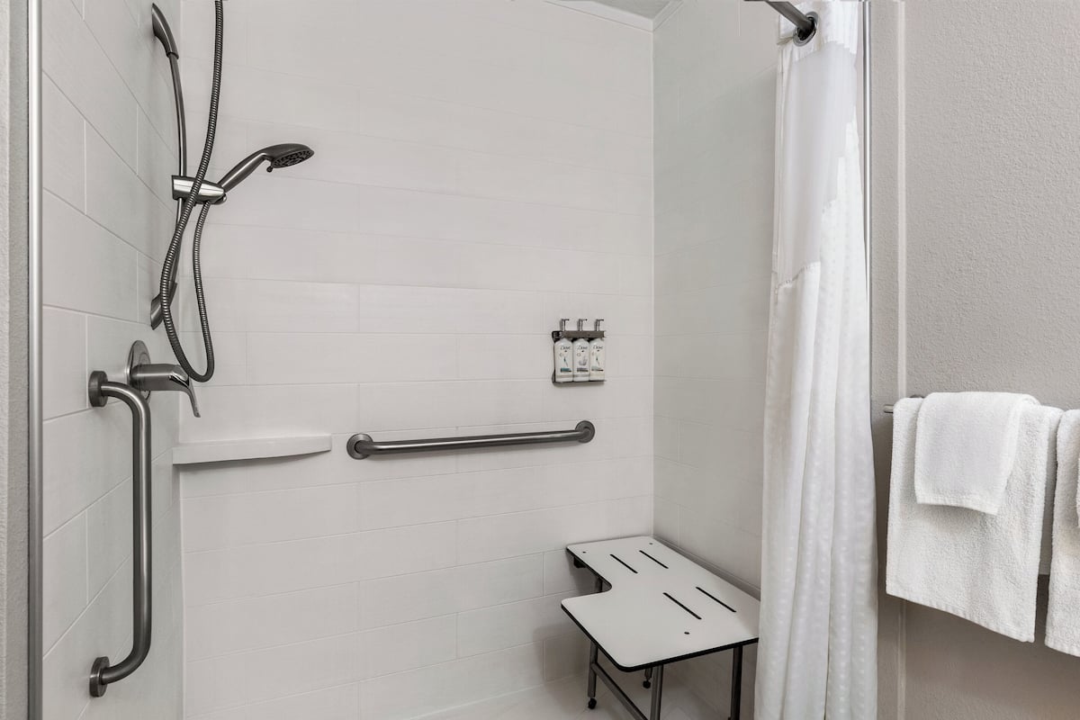 A shower area with a handheld showerhead, a handheld shower attachment, a grab bar, and a small bench.
