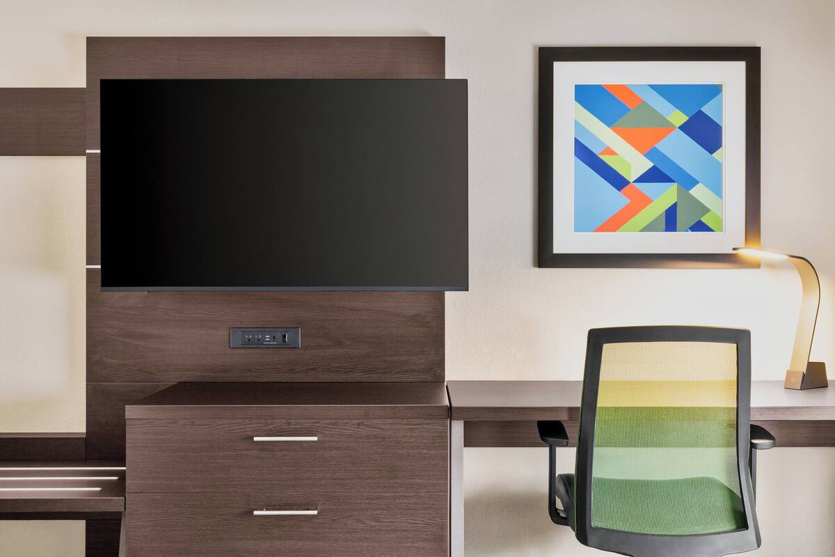 A modern office desk with a flat-screen TV, a framed abstract painting, and a desk lamp.