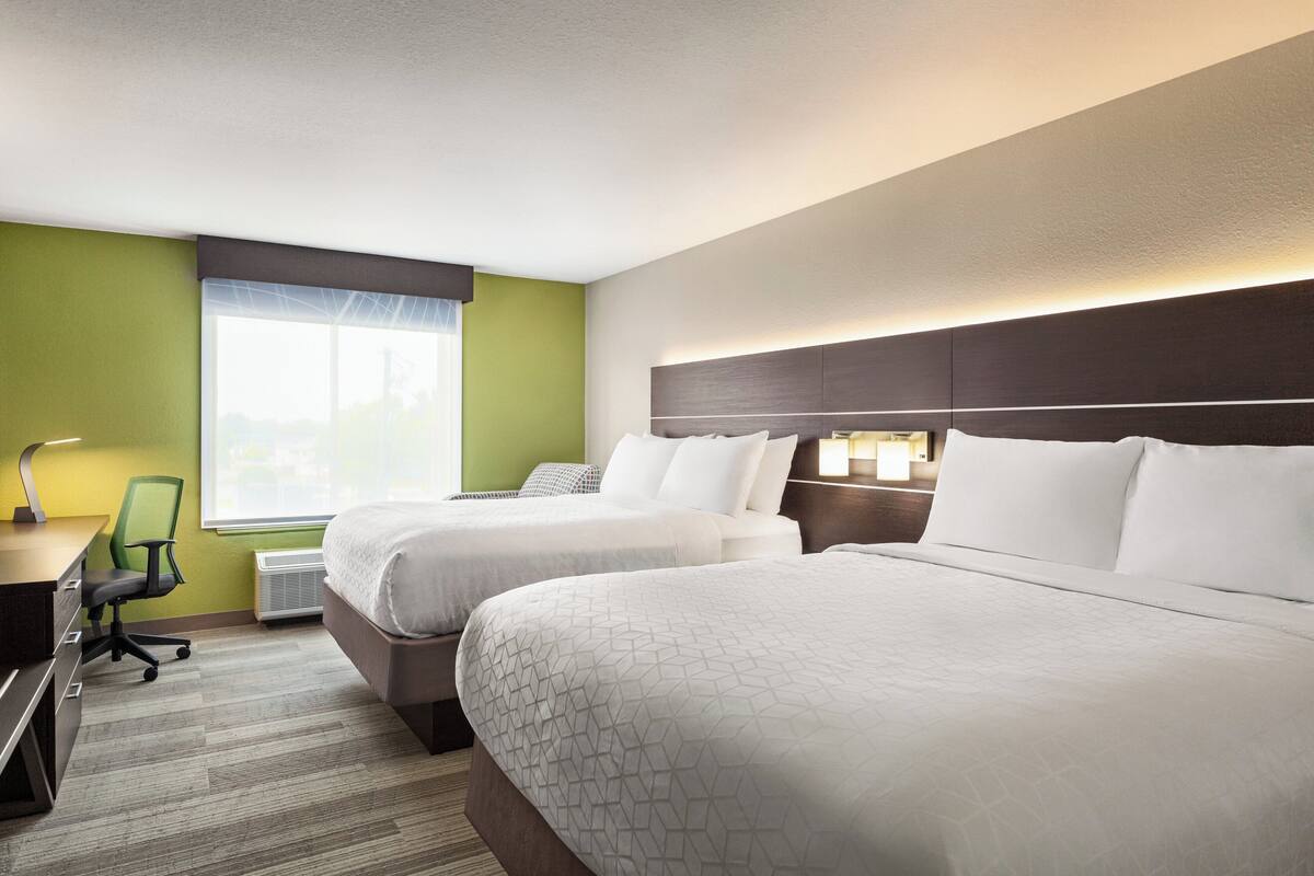 A hotel room with two beds, a desk, a chair, and a window with a view.