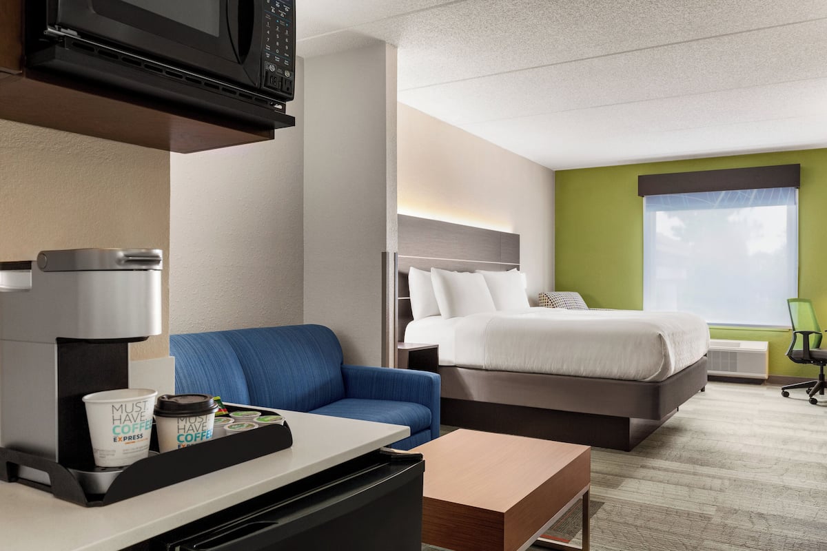 A hotel room with a bed, a desk with a coffee machine, a blue sofa, and a window with a view.