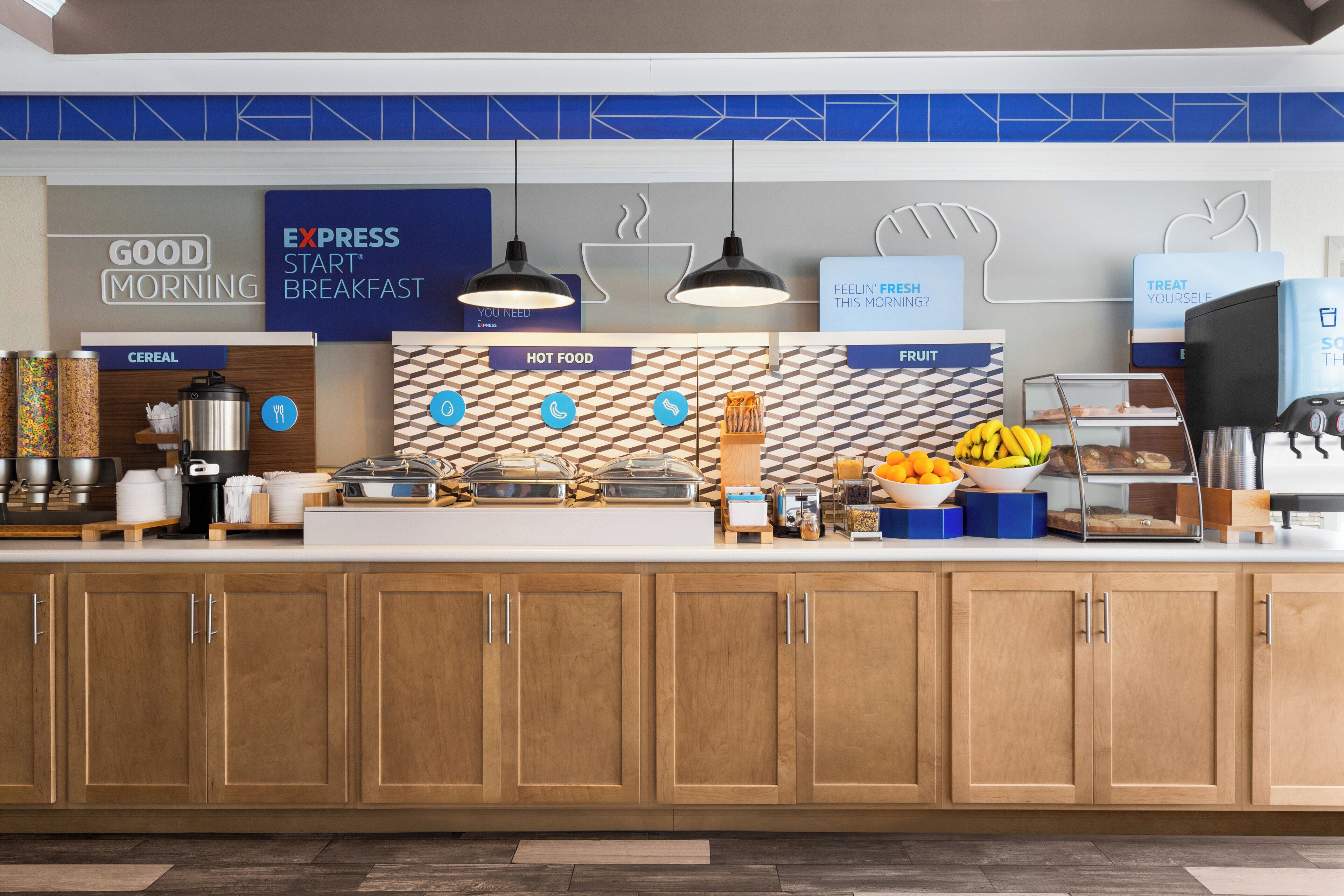 Zona de desayuno tipo buffet con secciones identificadas para cereales, comida caliente y fruta.
