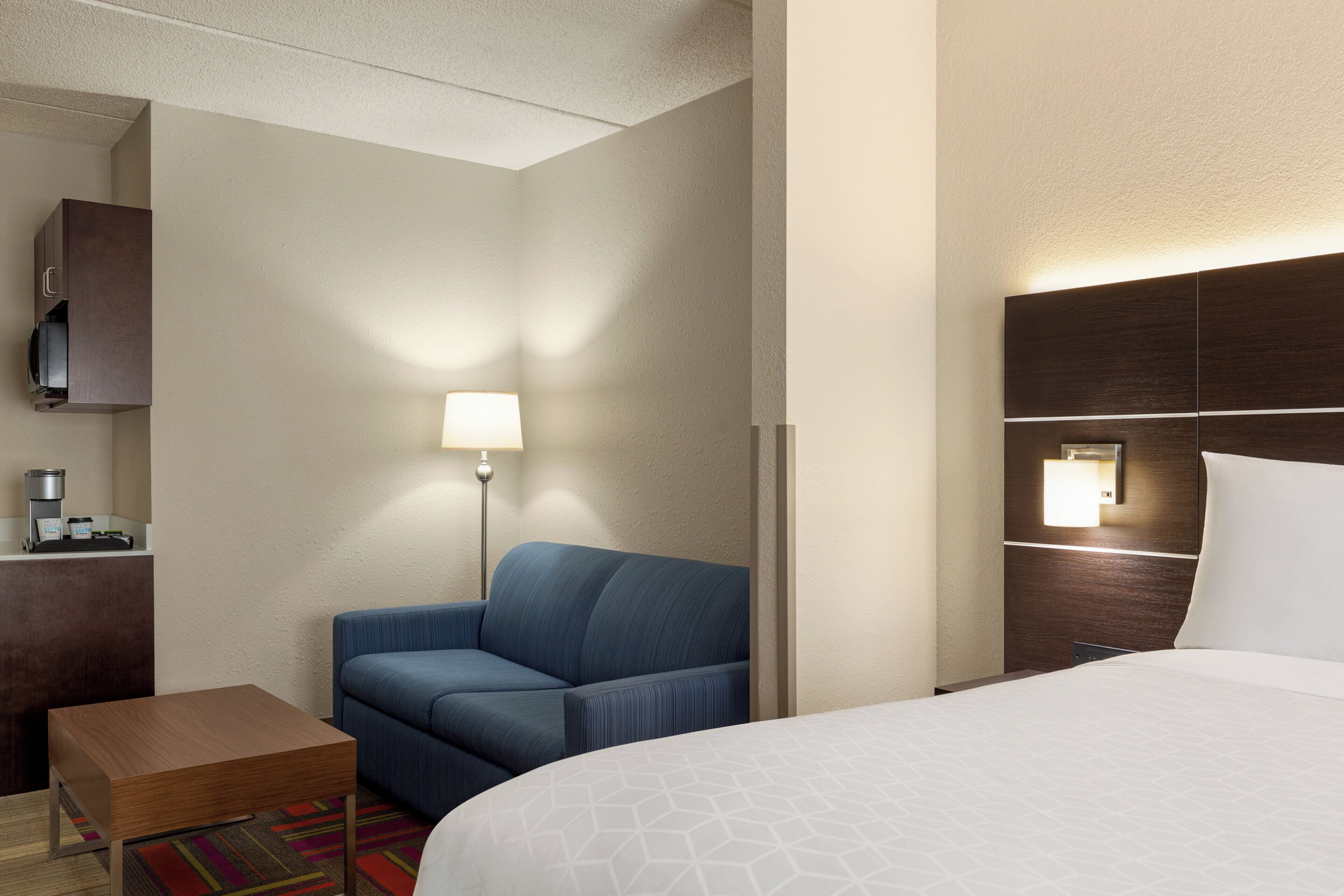 A hotel room with a bed, a sofa, a small table, a lamp, and a TV on a cabinet.