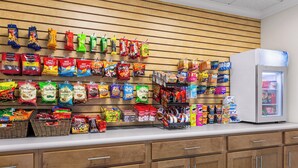 A snack display with various chips and snacks, a refrigerator, and wooden cabinets. - Holiday Inn Express & Suites Live Oak by IHG (Live Oak)