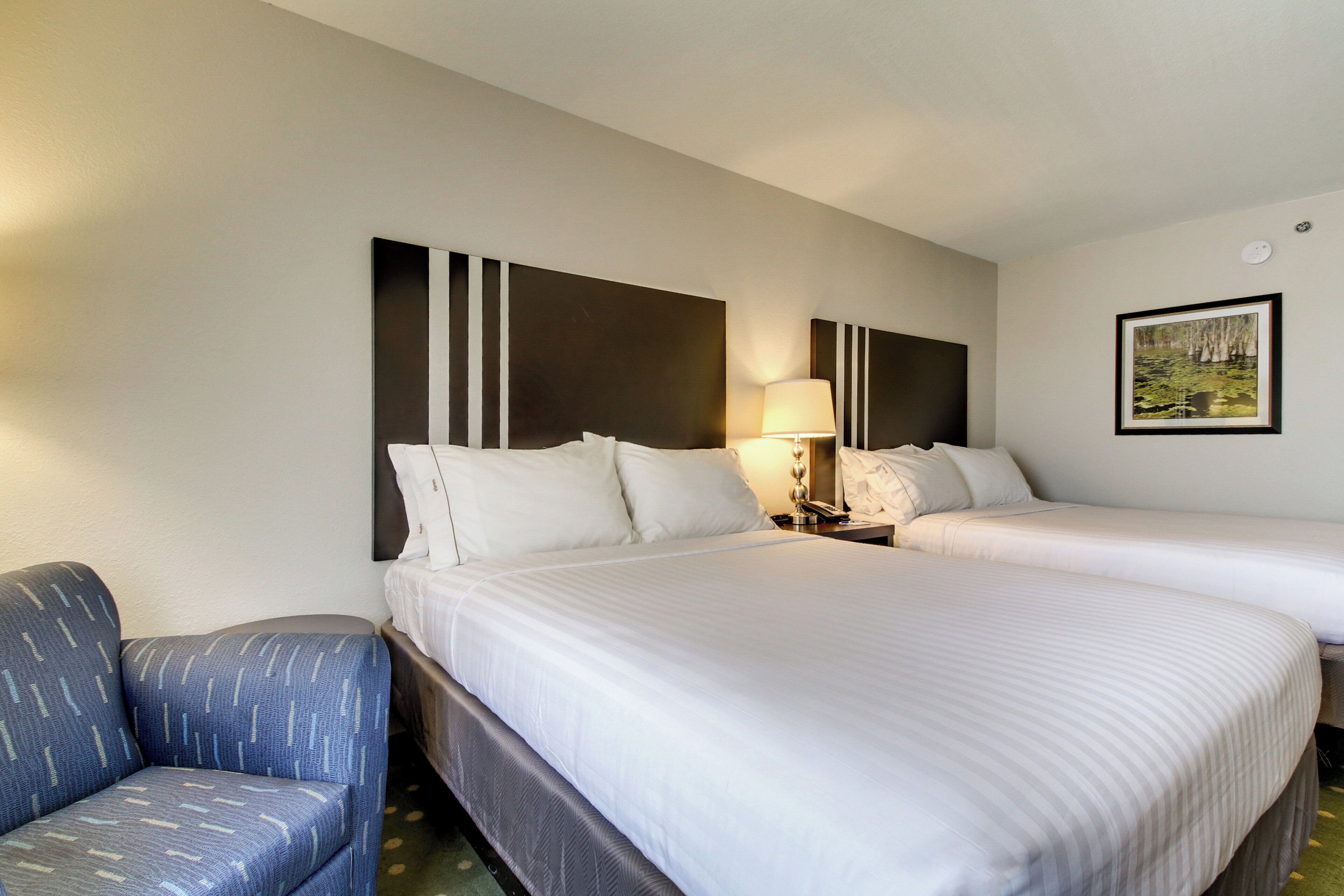Une chambre d’hôtel avec deux lits, une chaise, une lampe et un tableau encadré au mur.
