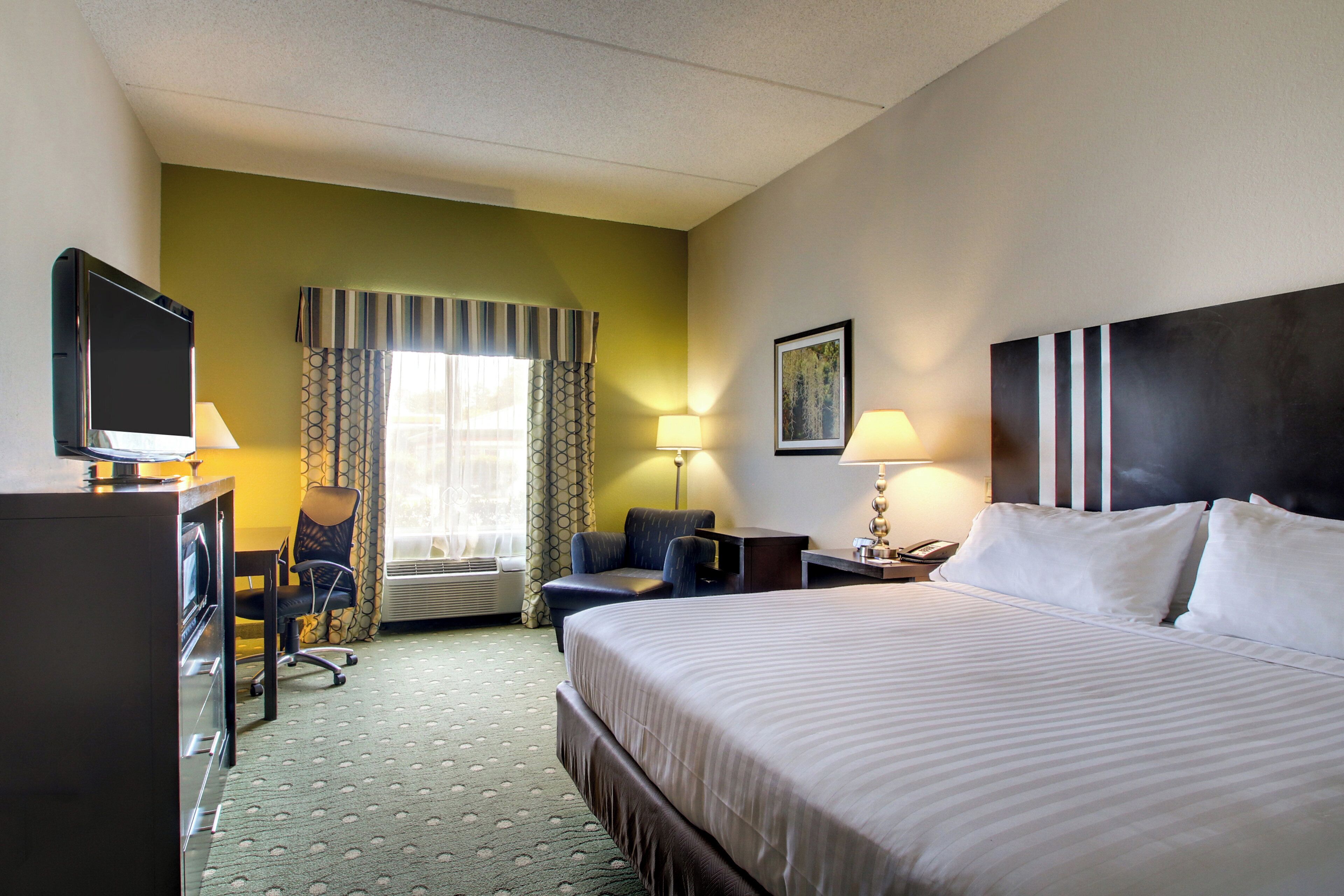 A hotel room with a bed, desk, chair, television, and two lamps.