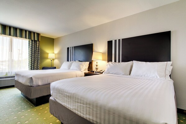 Habitación de hotel con dos camas, un ventanal con cortinas y un televisor montado en la pared.