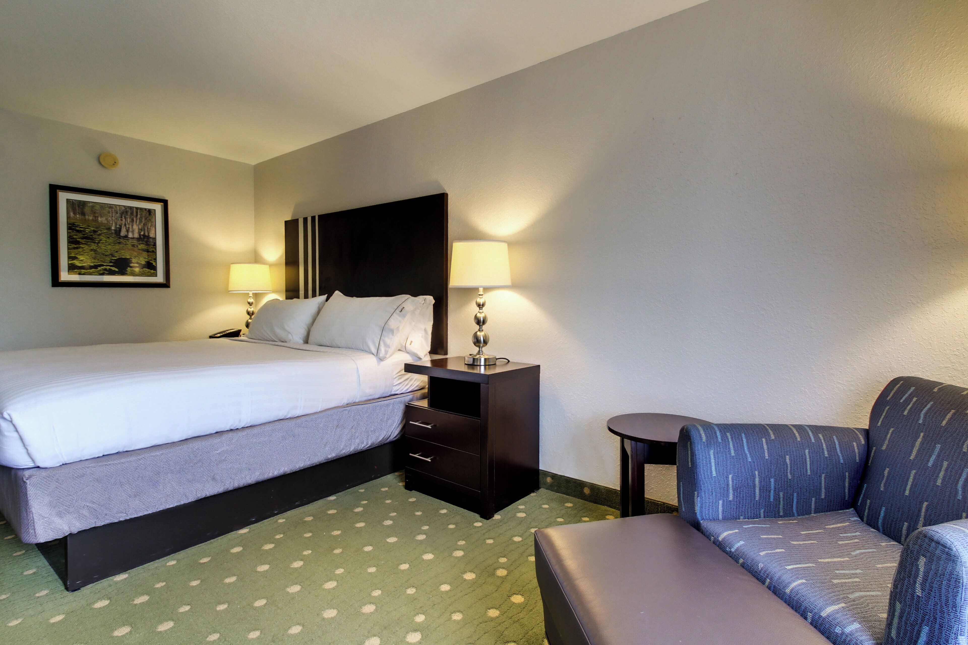A hotel room with a bed, a desk, a chair, and a small table.