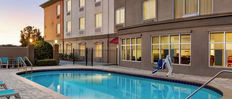 A swimming pool with lounge chairs, a covered seating area, and a building with multiple windows and a red awning.