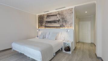 A modern bedroom with a large bed, a headboard with a rustic wall art, a bedside table with a lamp, and a small storage box.