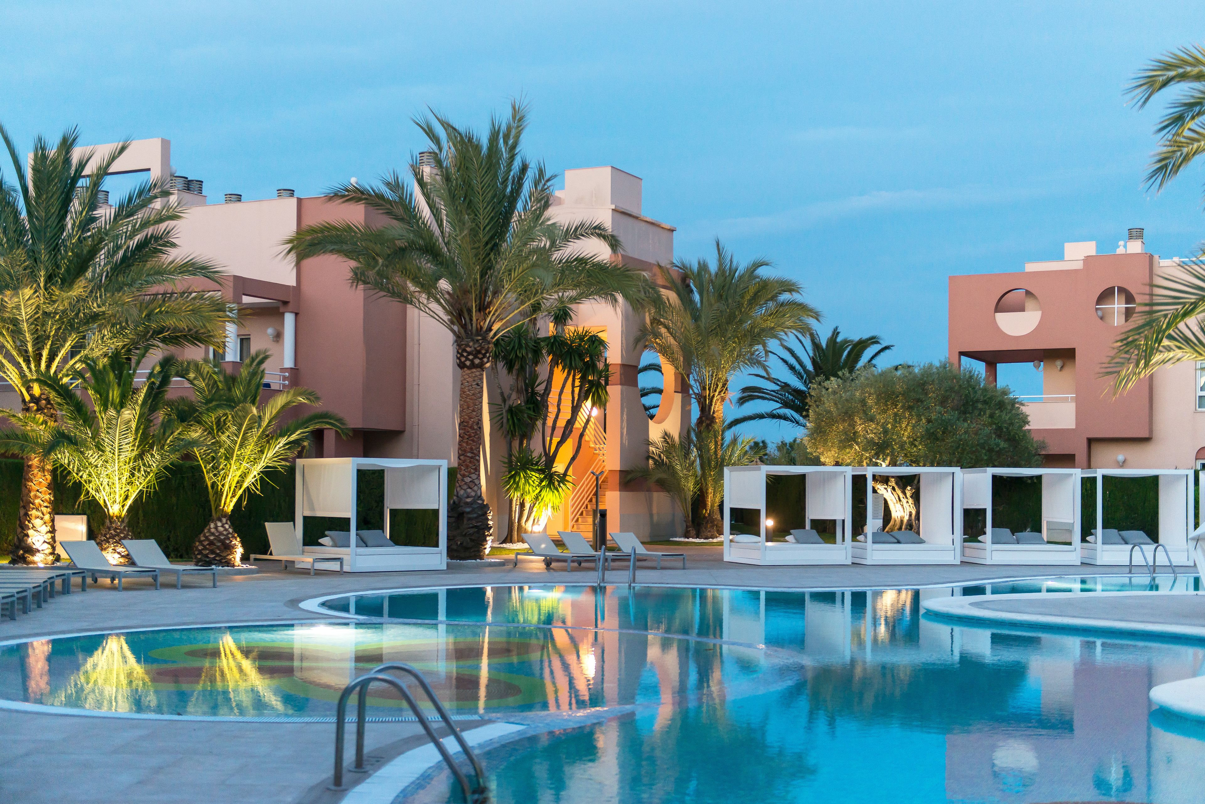 Una piscina con lettini e palme, circondata da edifici in stile architettonico moderno.