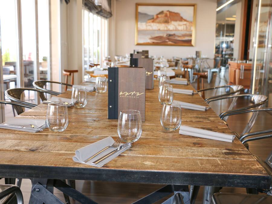 Un restaurante con mesas de madera y sillas de metal, un atril con la carta y un cuadro en la pared.