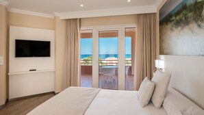 Ett hotellrum med en stor säng, en platt-TV som är monterad på väggen, en balkong med utsikt över havet och en tavla på väggen.
