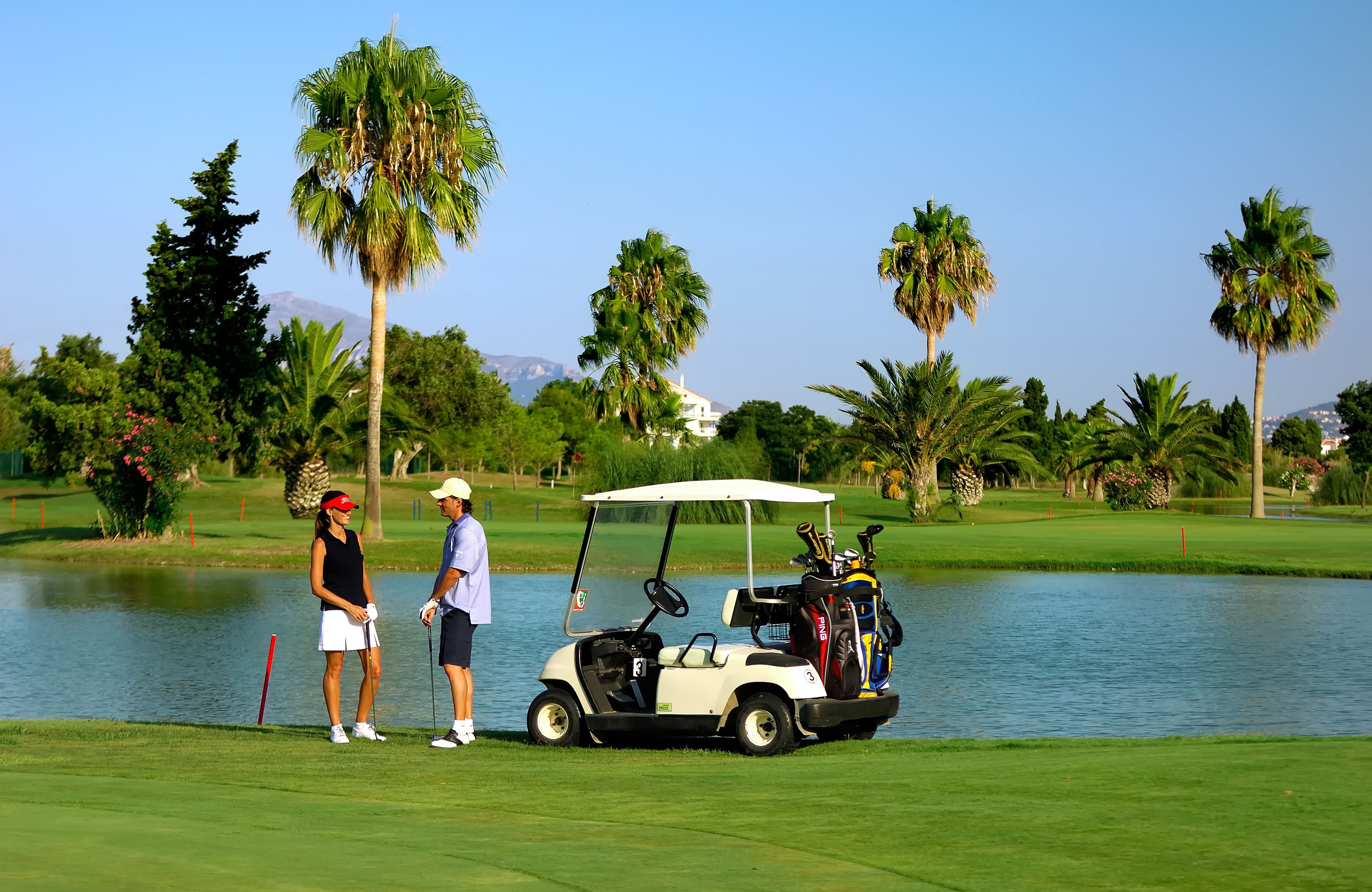 Un campo de golf con un cuerpo de agua, palmeras y un carrito de golf.