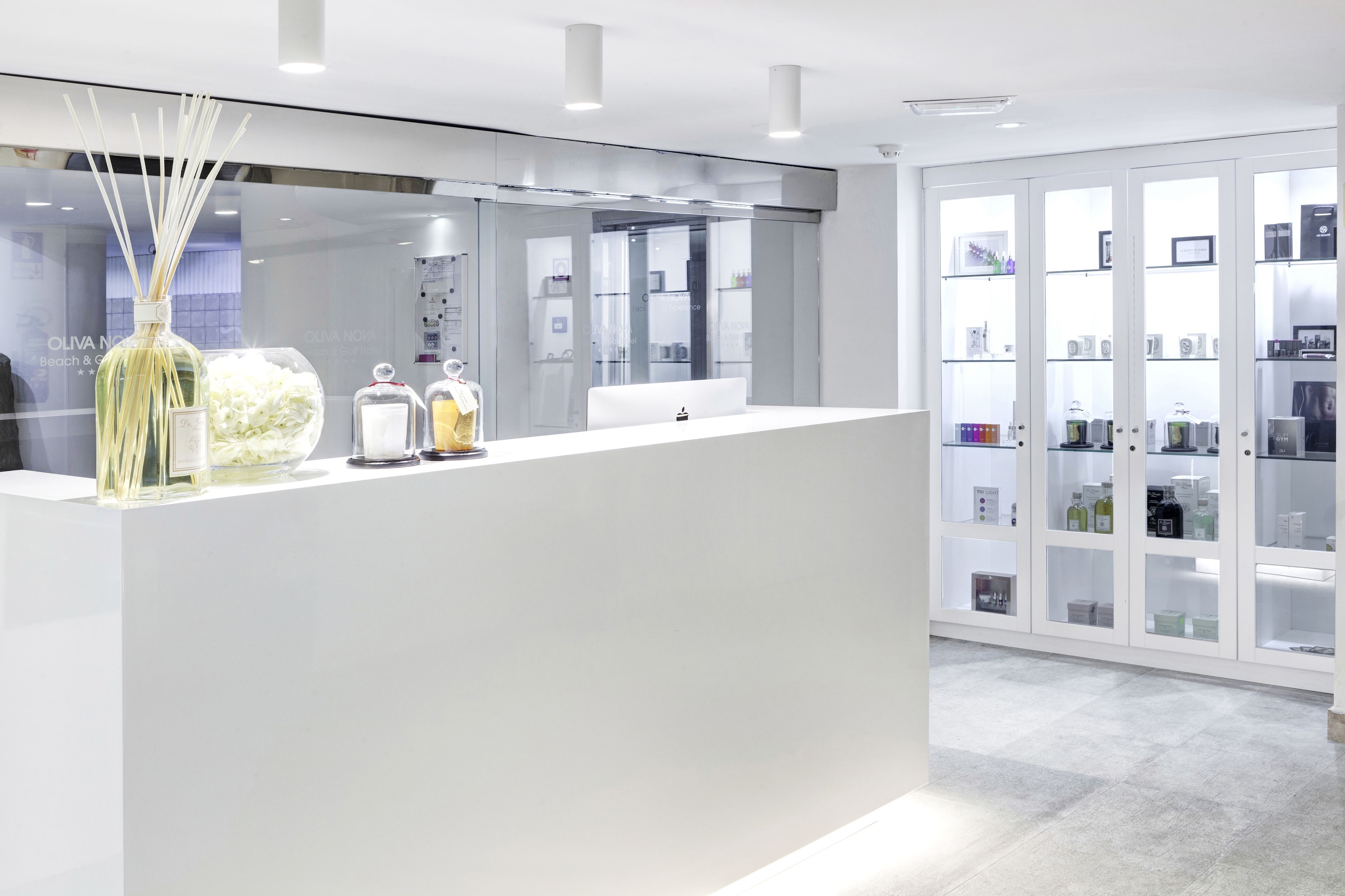 A modern reception area with a white counter, glass display cabinets, and a large vase with reed sticks.