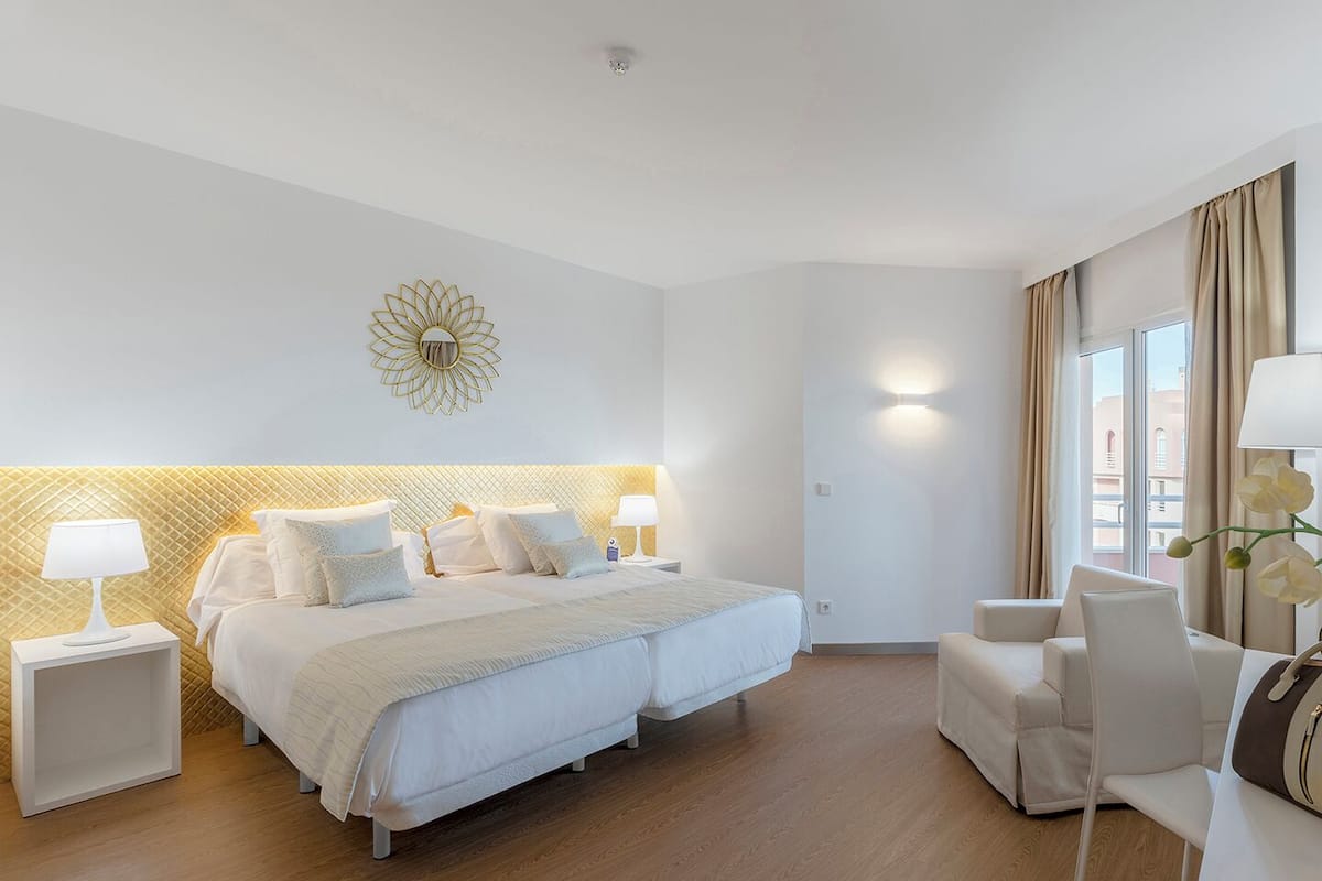 Une chambre d’hôtel avec un lit double, deux tables de chevet avec des lampes, un canapé et un élément décoratif mural.