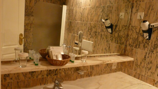 Un baño con lavamanos de mármol, un espejo, toallero y repisa con artículos de aseo.