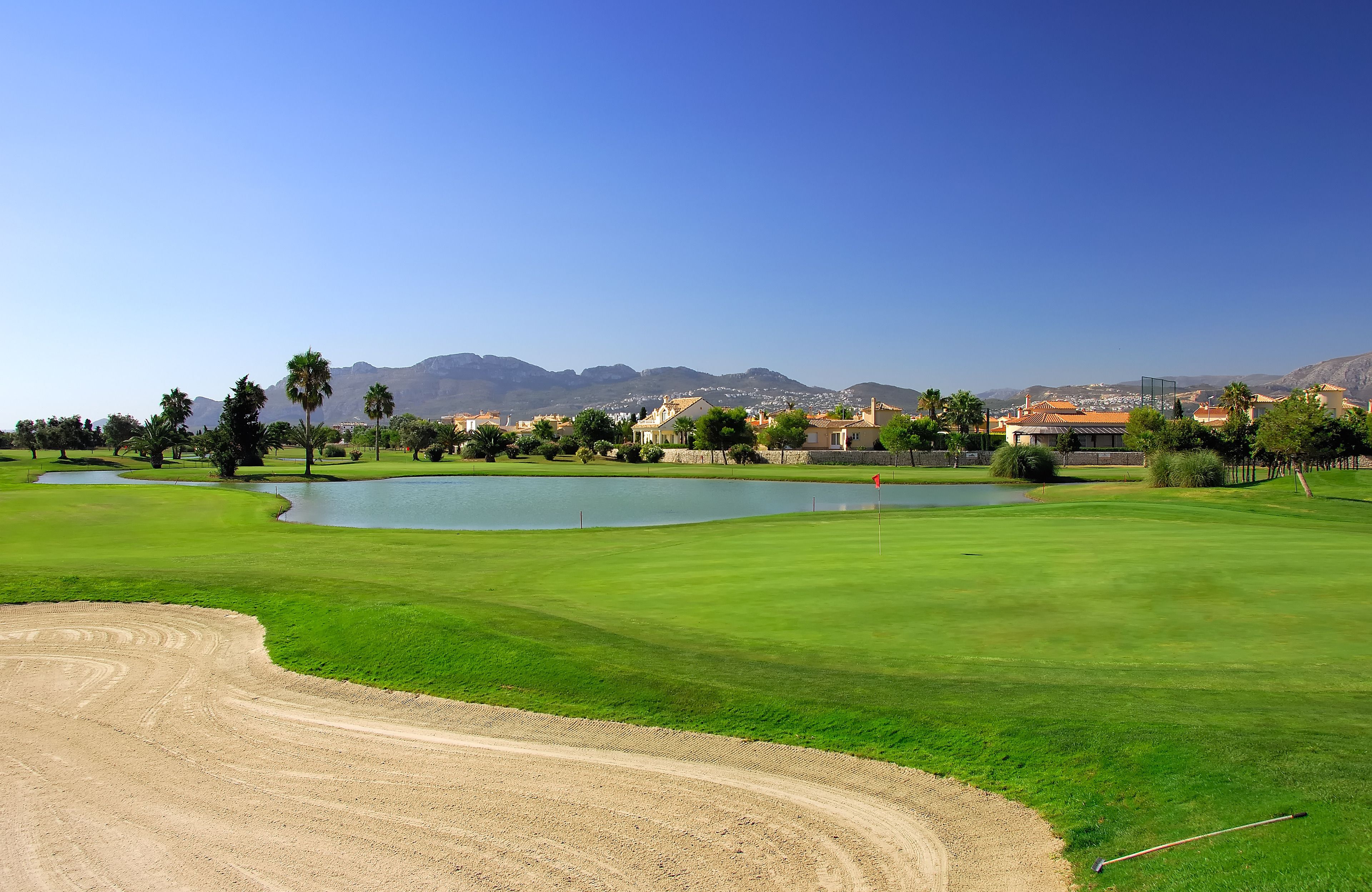 A golf course with a pond, sand bunkers, and a clear view of mountains in the background.