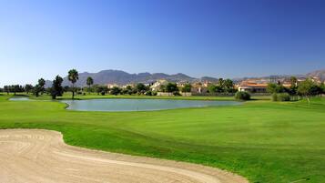 A golf course with a pond, sand bunkers, and a clear view of mountains in the background.