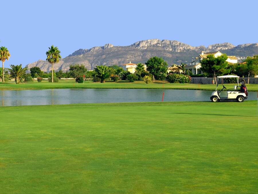 A golf course with a lake, palm trees, and mountains in the background.