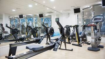 A gym with various exercise machines, including rowing machines and treadmills, arranged in a spacious layout.