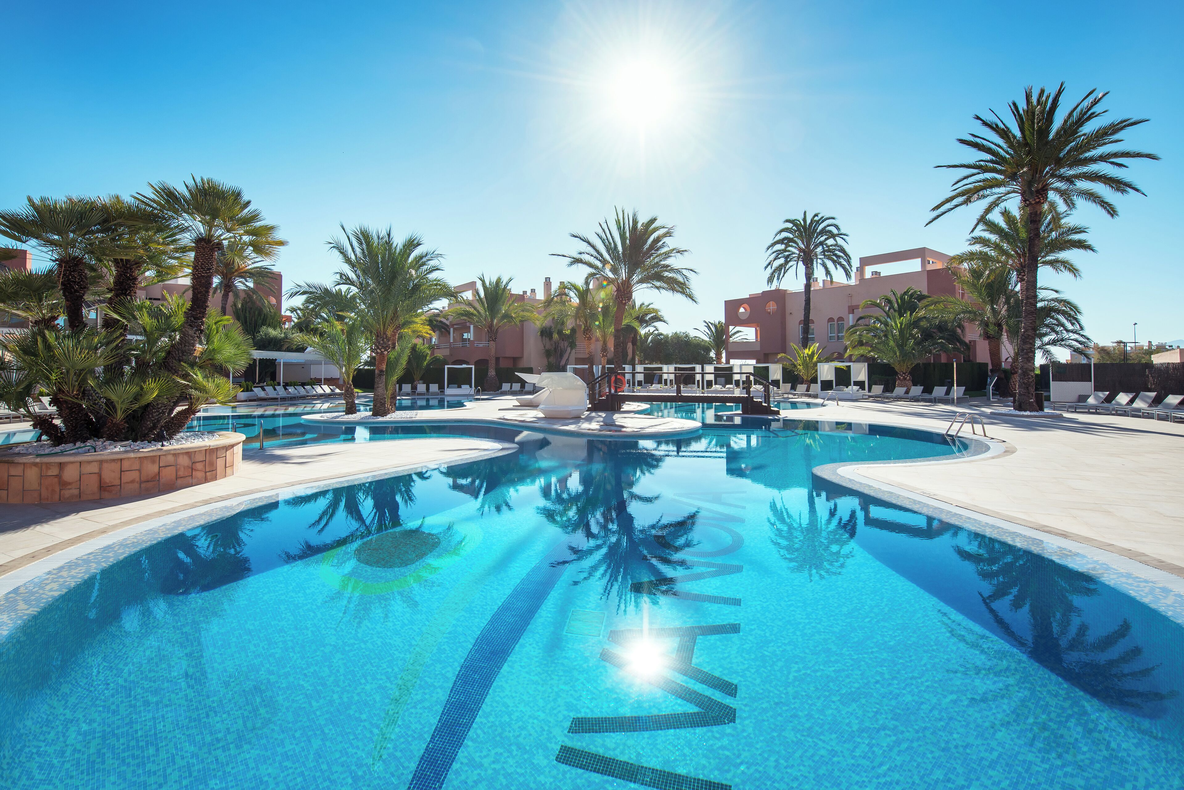 A clear blue pool surrounded by palm trees and modern buildings.