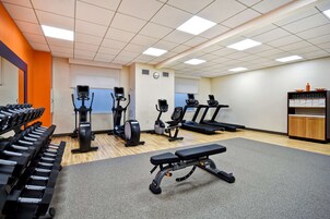 Un gimnasio con equipo de ejercicio variado, incluyendo cintas de correr, elípticas y pesas libres.