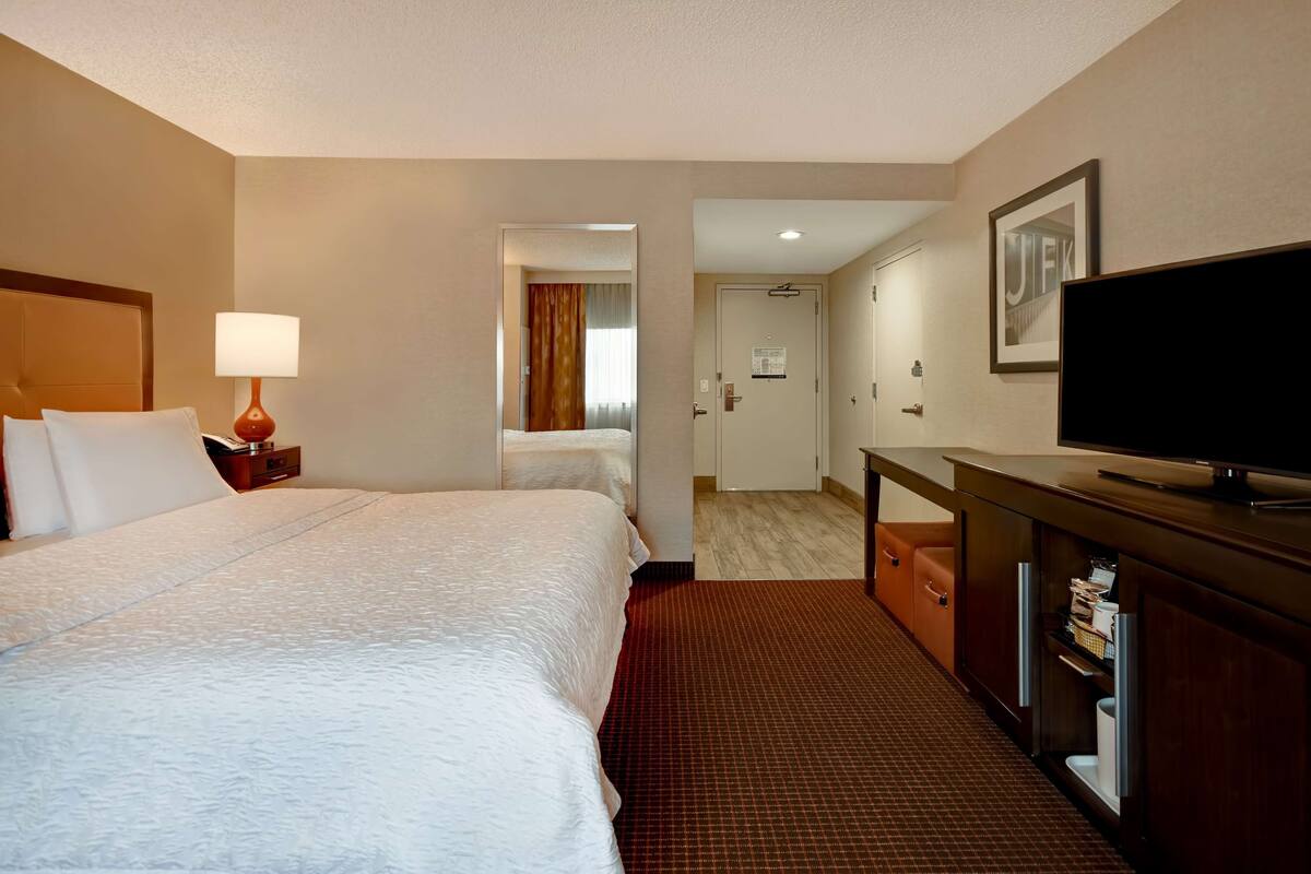 Ein Hotelzimmer mit einem großen Bett, einem Schreibtisch mit Fernseher und einer Tür zu einem Badezimmer.