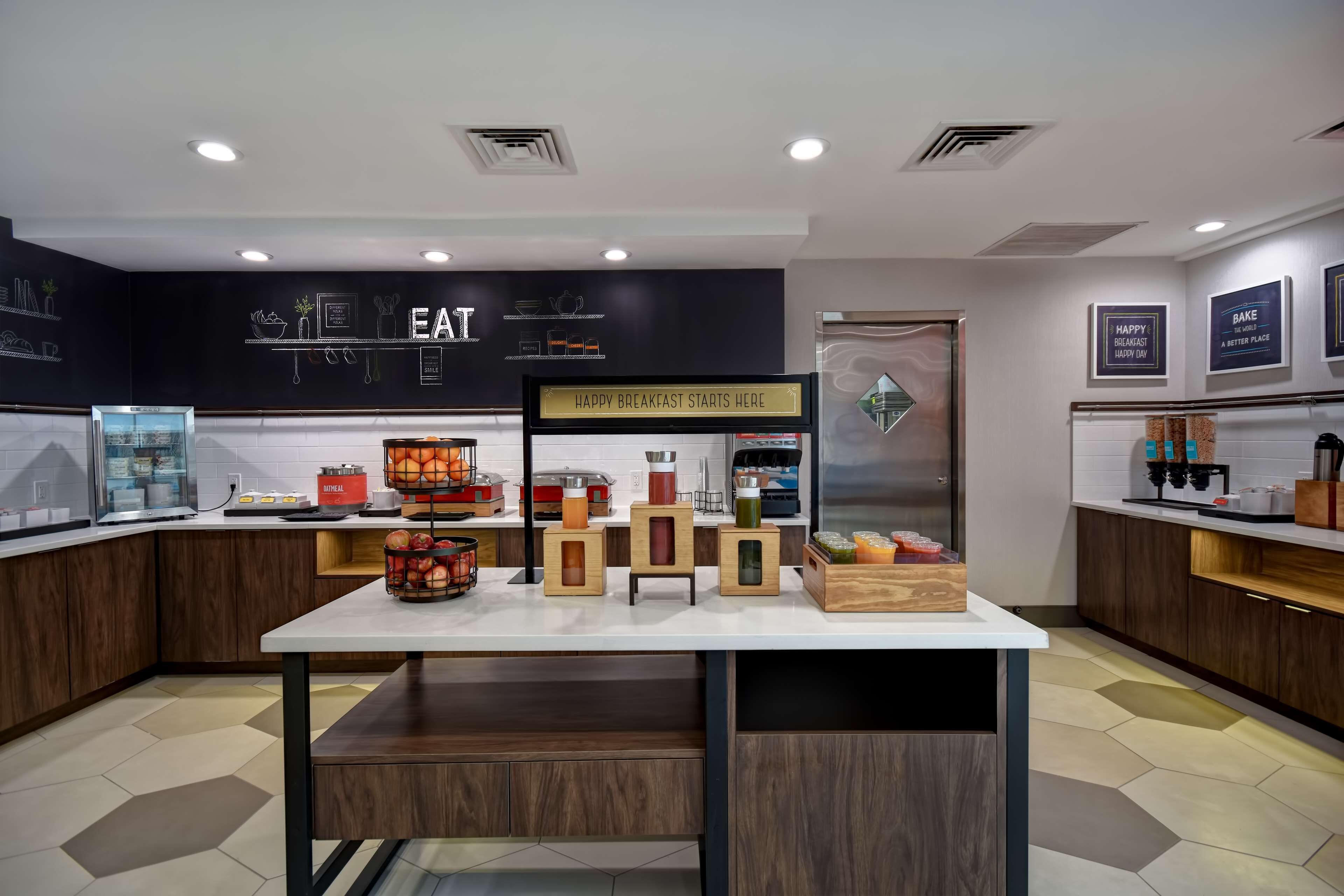 A modern kitchen with a central island, wooden cabinets, and a sign that reads "HAPPY BREAKFAST STARTS HERE".