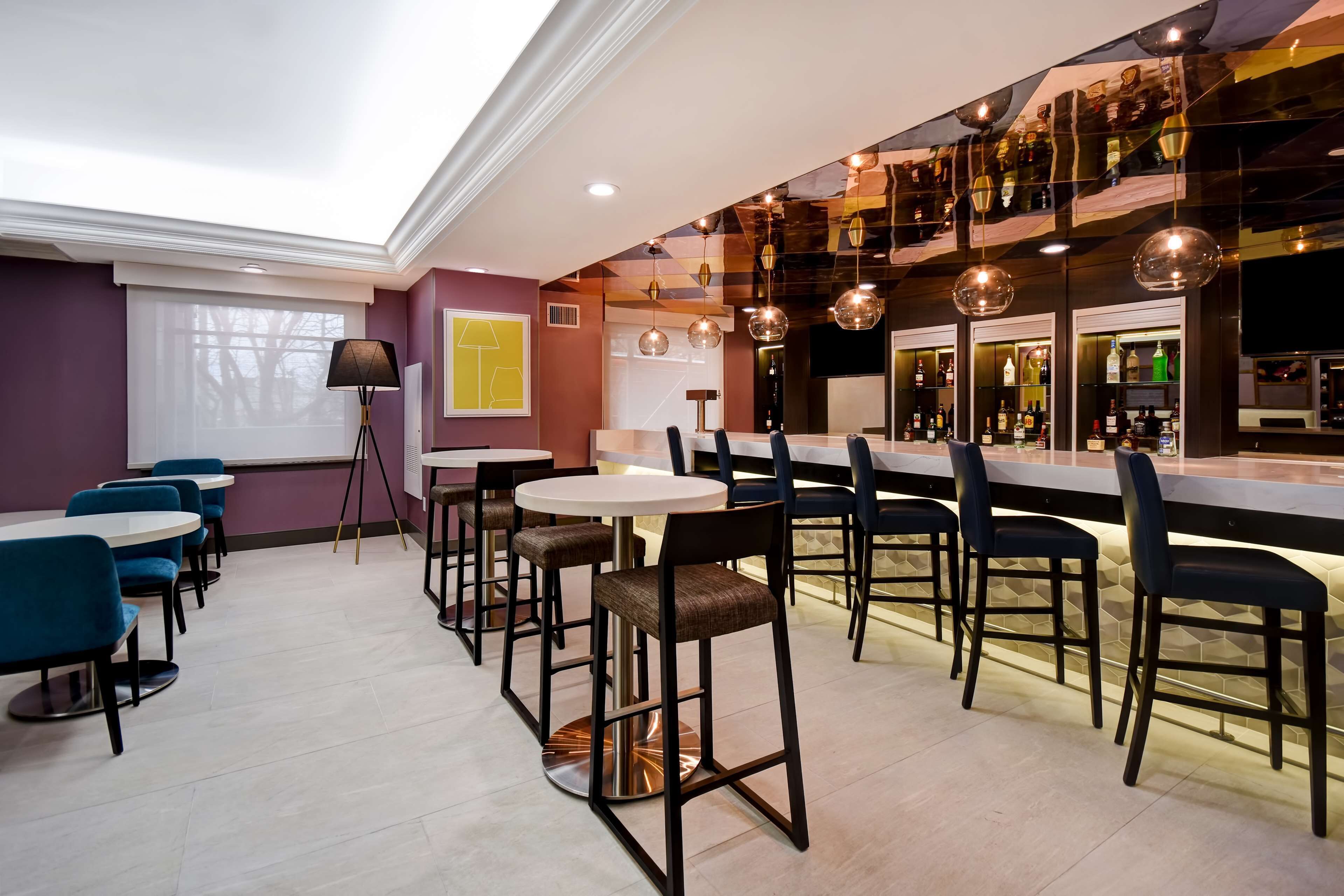 A modern bar area with round tables, bar stools, and a variety of bottles on shelves.