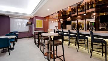 A modern bar area with round tables, bar stools, and a variety of bottles on shelves.