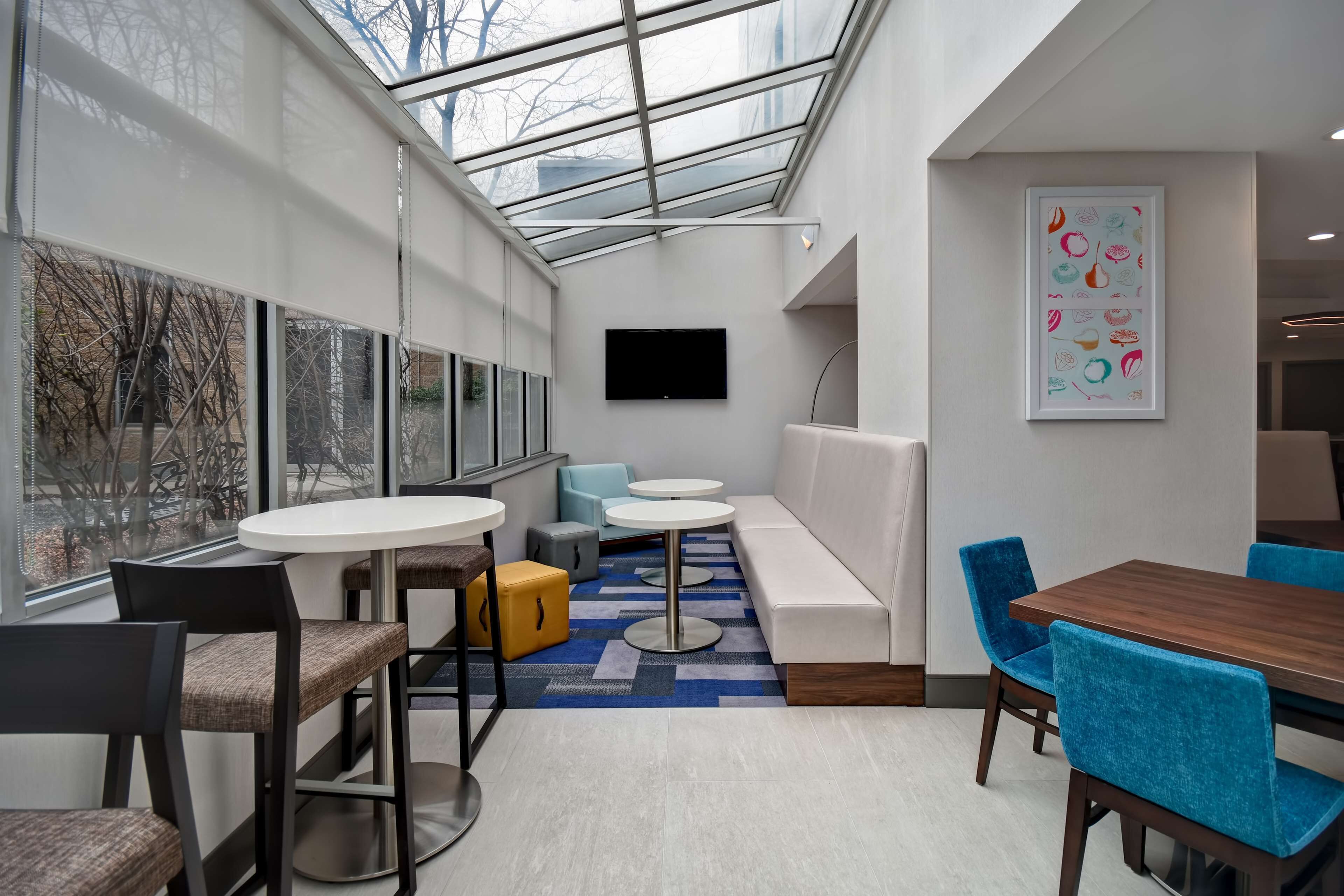 A modern interior with a glass ceiling, a flat-screen TV, a sofa, a dining table with chairs, and a colorful abstract painting.