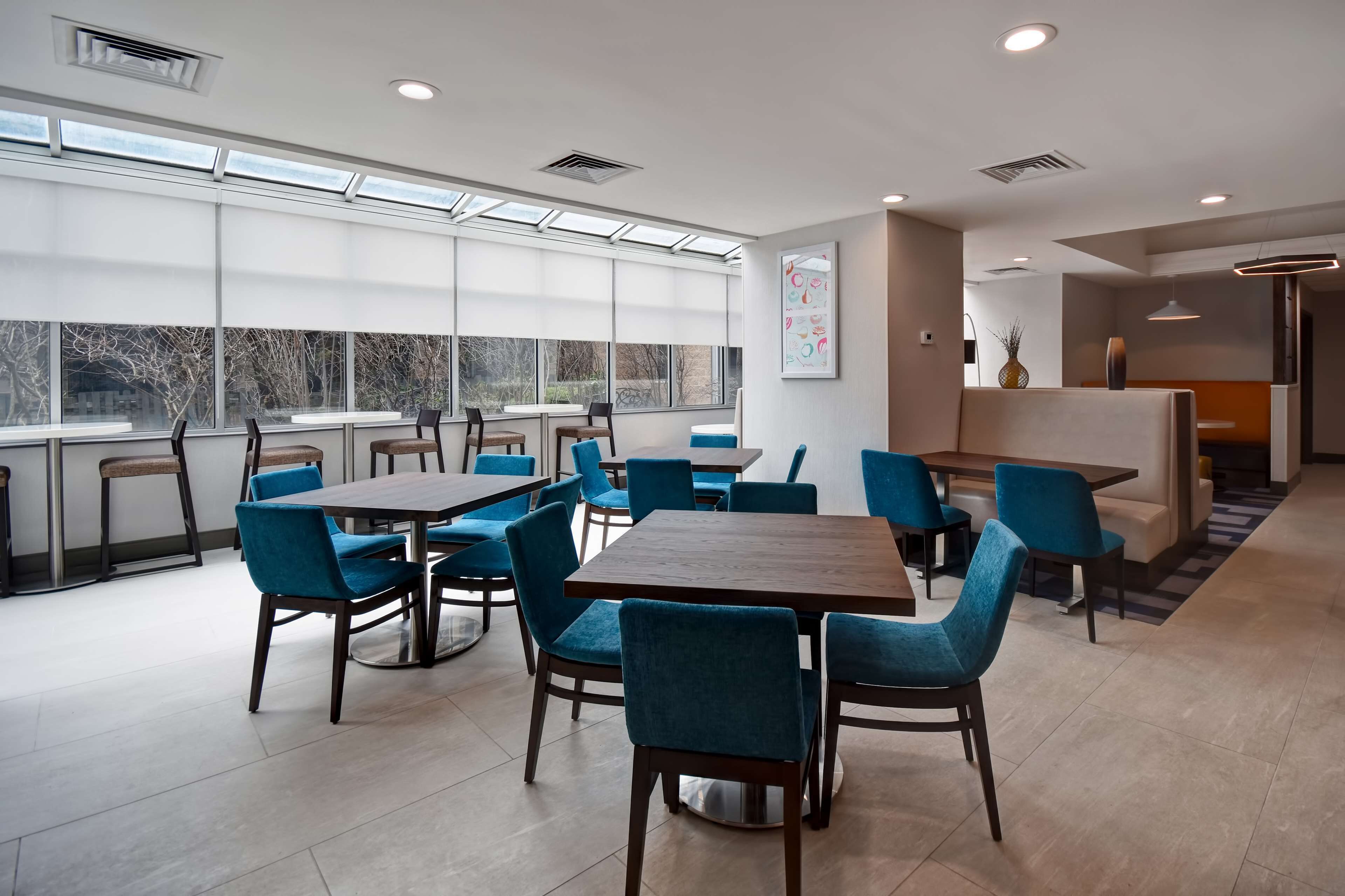 Un espace de restauration moderne, doté de plusieurs tables et chaises, de grandes fenêtres et offrant une vue sur l’extérieur.