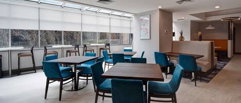 A modern dining area with multiple tables and chairs, large windows, and a view of the outdoors.