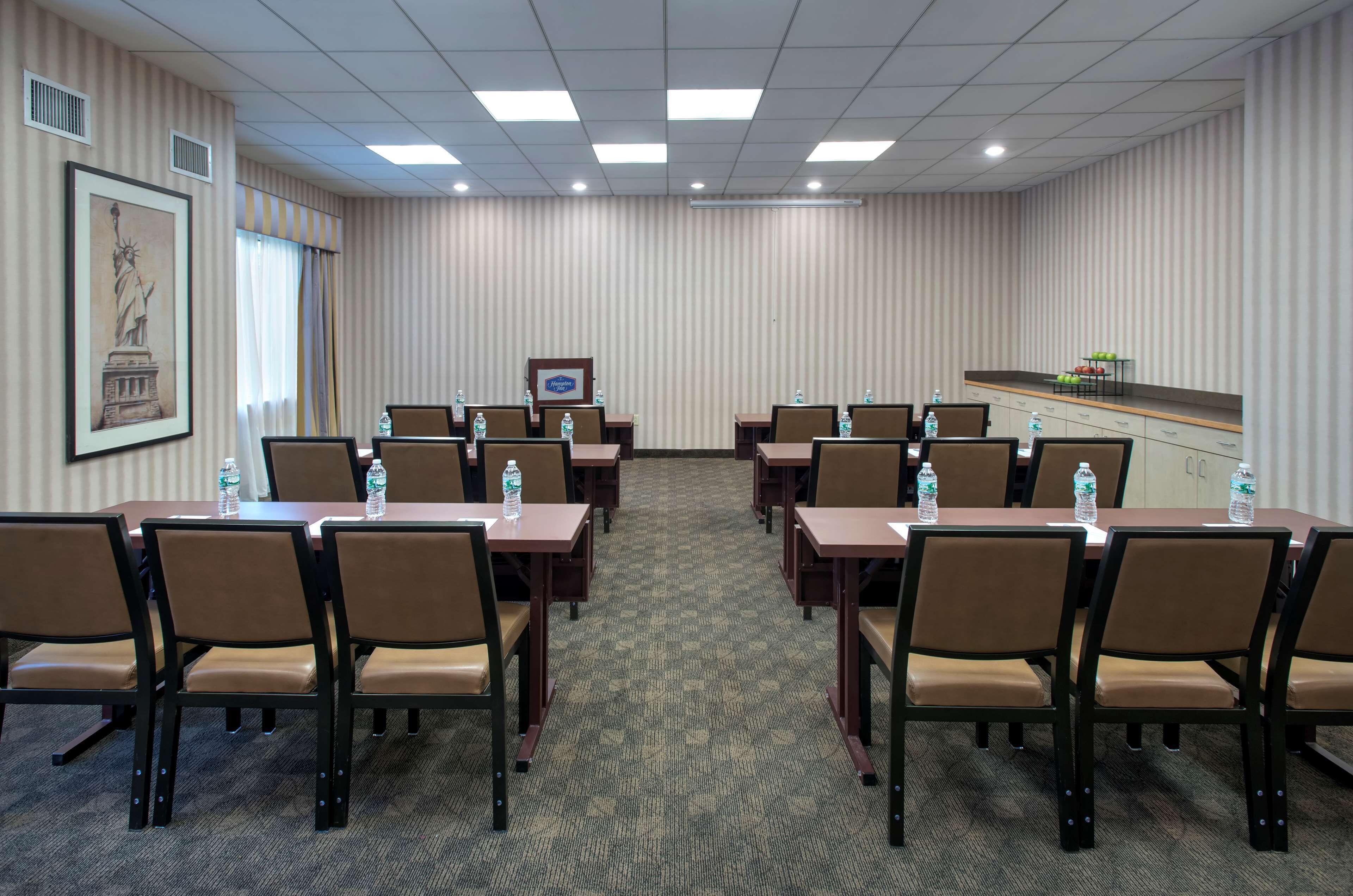 A conference room with multiple tables and chairs, a framed picture of the Statue of Liberty, and a water dispenser on each table.