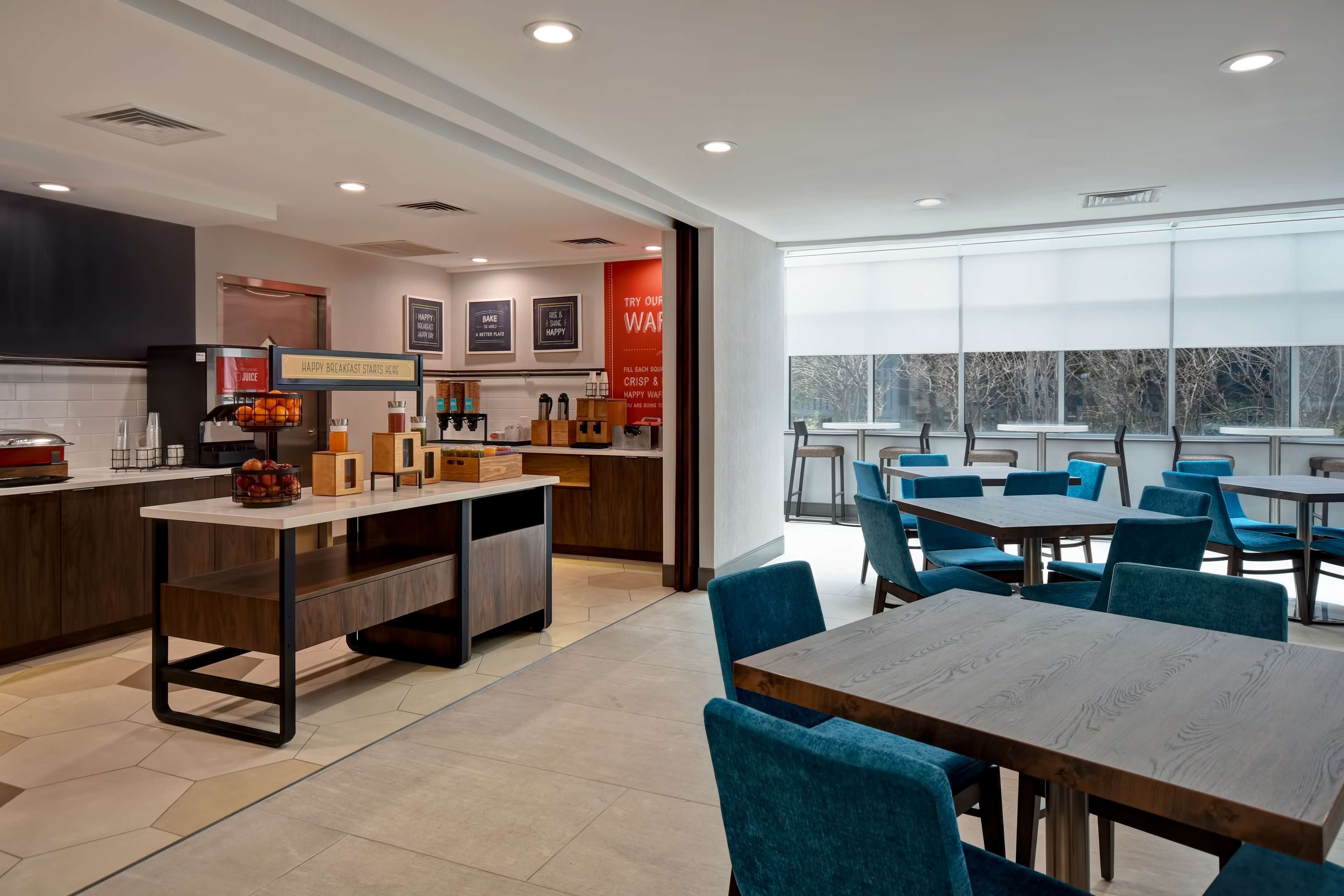 A modern breakfast area with a counter, seating, and a view of trees through large windows.
