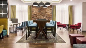 A modern hotel lobby with a central wooden table surrounded by blue and red chairs, a stone wall, and a chandelier. - Hampton Inn Quakertown (Quakertown)