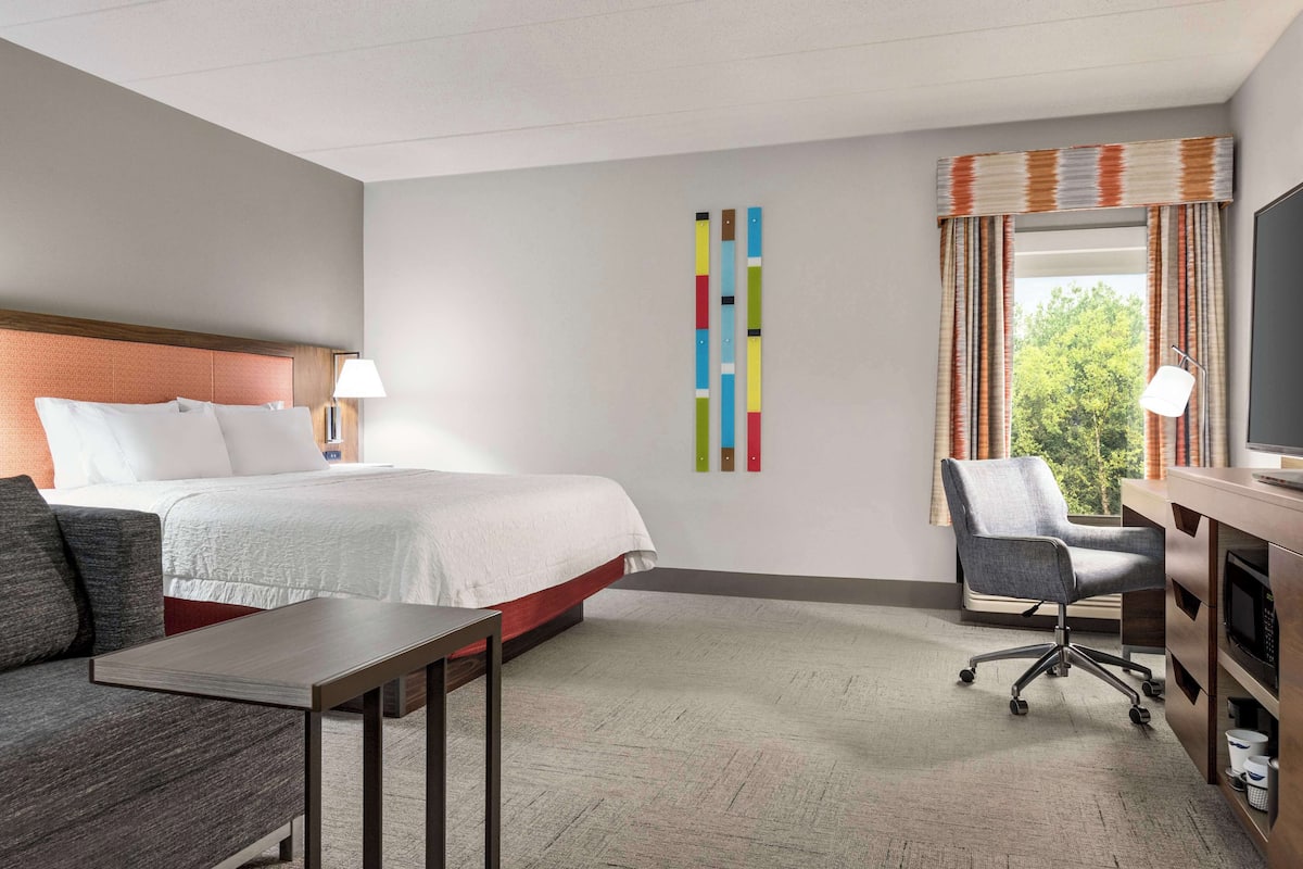 A hotel room with a bed, a desk, a chair, a TV, and a window with curtains.