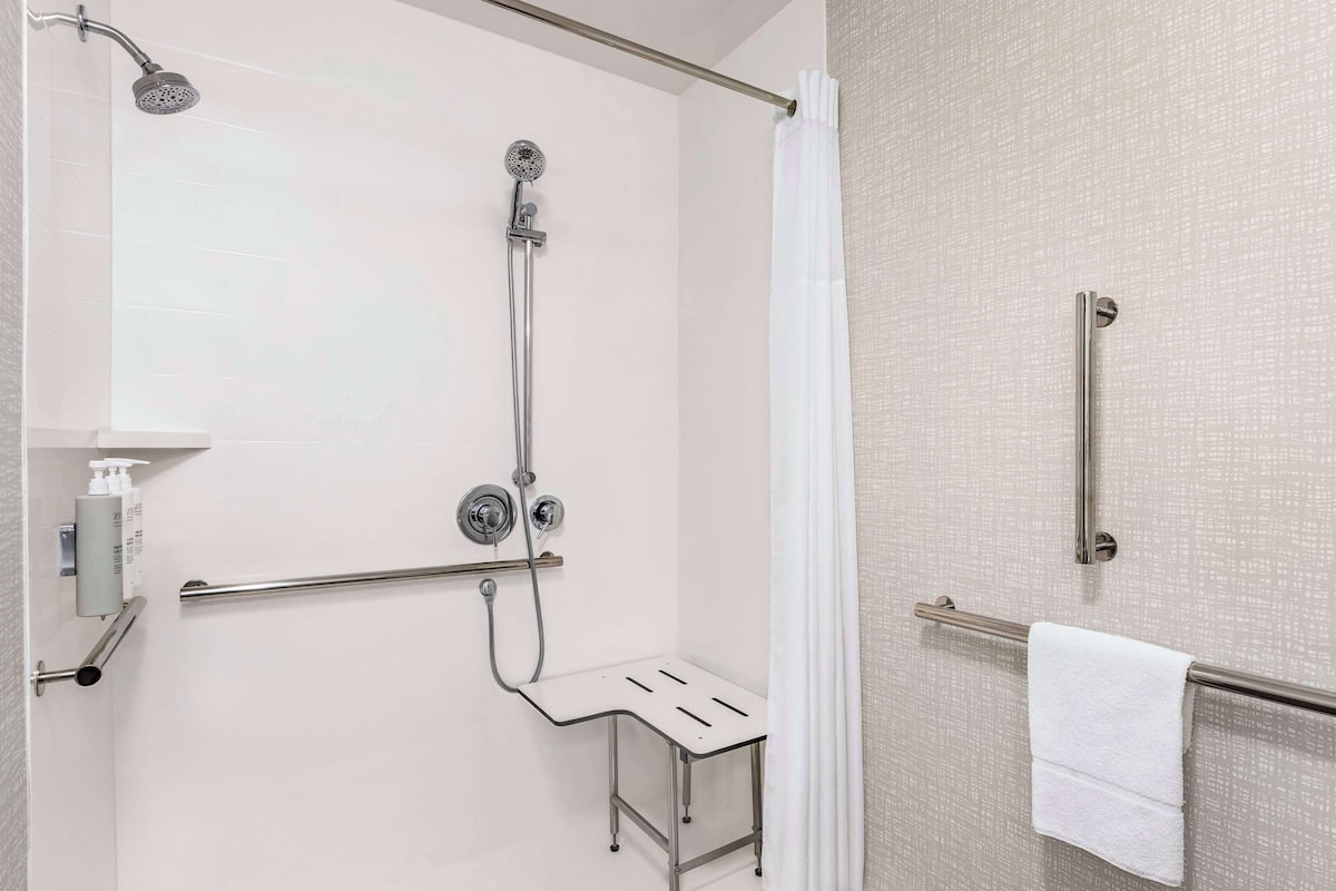 A modern bathroom with a shower, grab bars, and a towel rack.