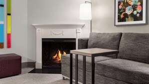 A modern living room with a fireplace, a gray sofa, a small table, and a colorful abstract painting on the wall. - Hampton Inn Quakertown (Quakertown)
