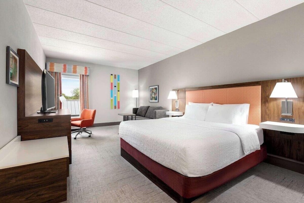 A modern hotel room with a large bed, a desk, a chair, and a TV.