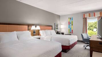 A hotel room with two beds, a desk, a chair, and a window with curtains.