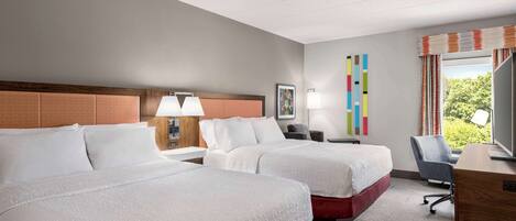 A hotel room with two beds, a desk, a chair, and a window with curtains.