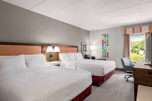 A hotel room with two beds, a desk, a chair, and a window with curtains.