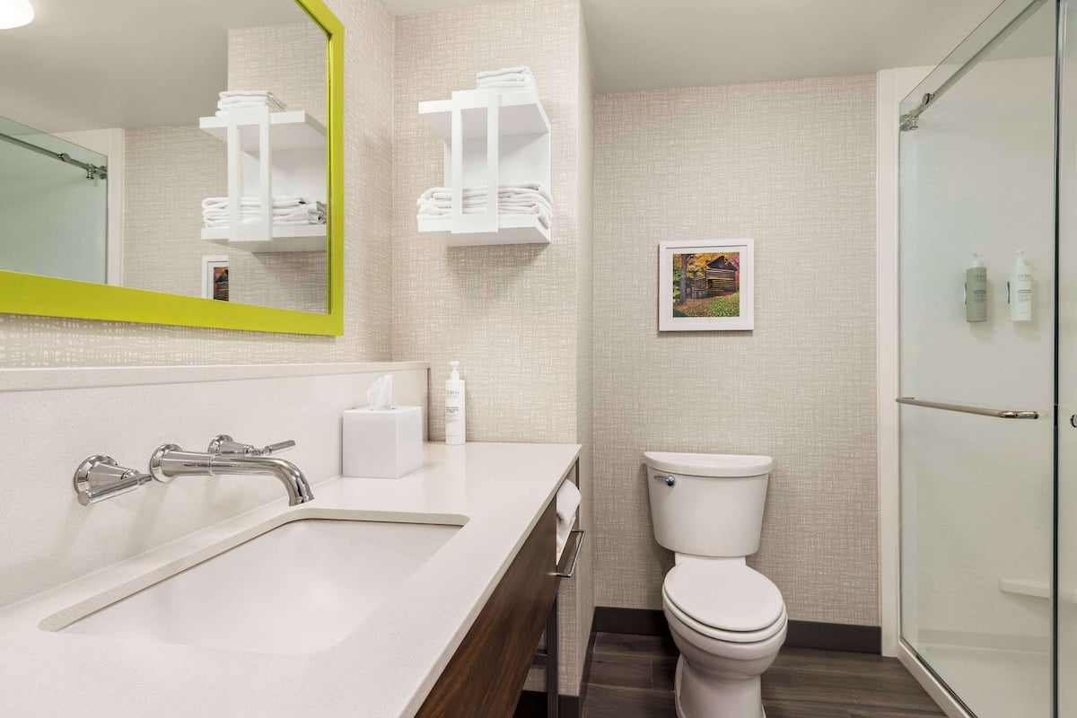 A modern bathroom with a white sink, a mirror with a yellow frame, a toilet, and a shower area.